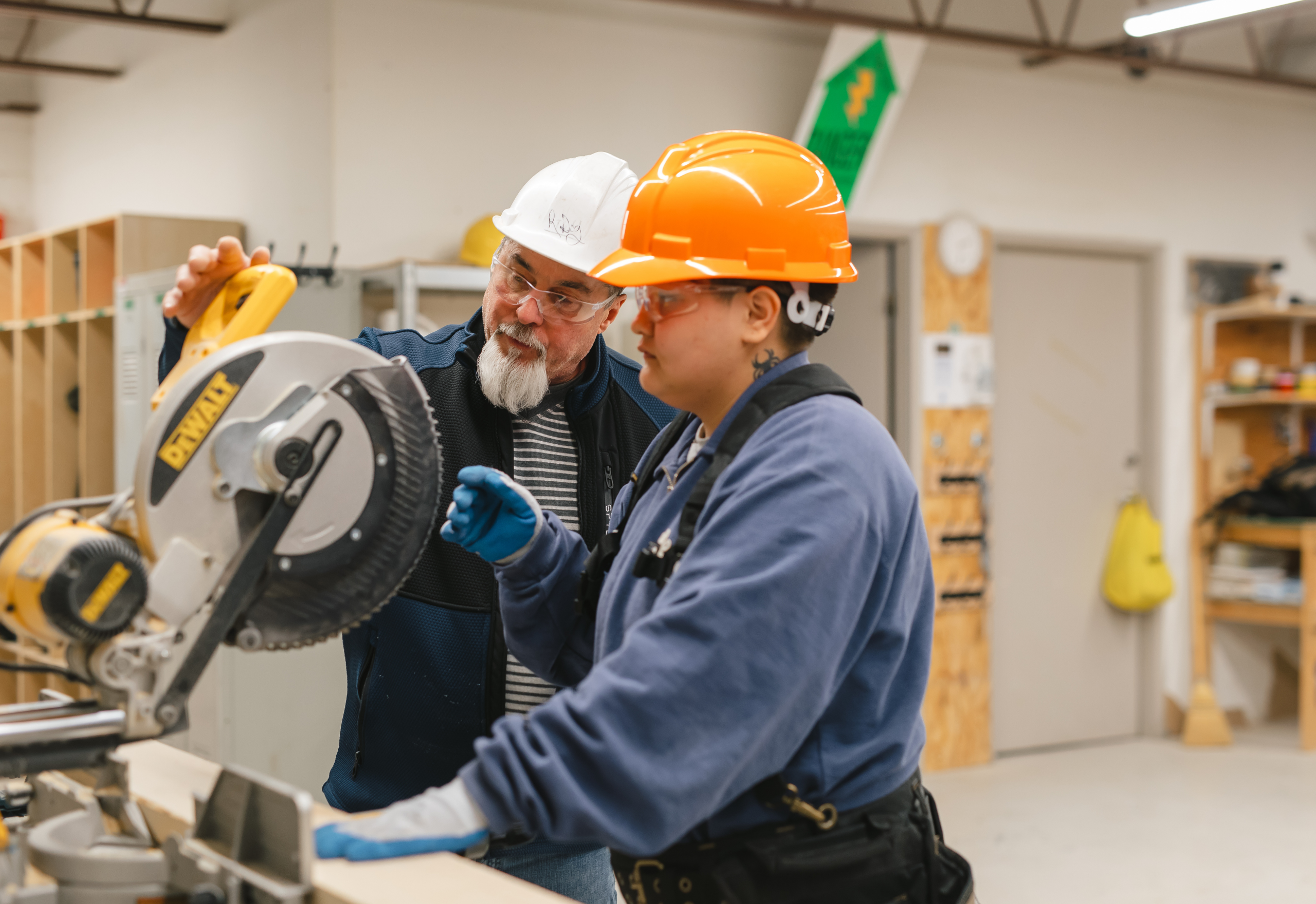 Construction student in safety gear learning safe saw operation from a facilitator