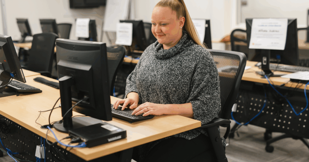 An admin student sits in front of a keyboard and monitor during class