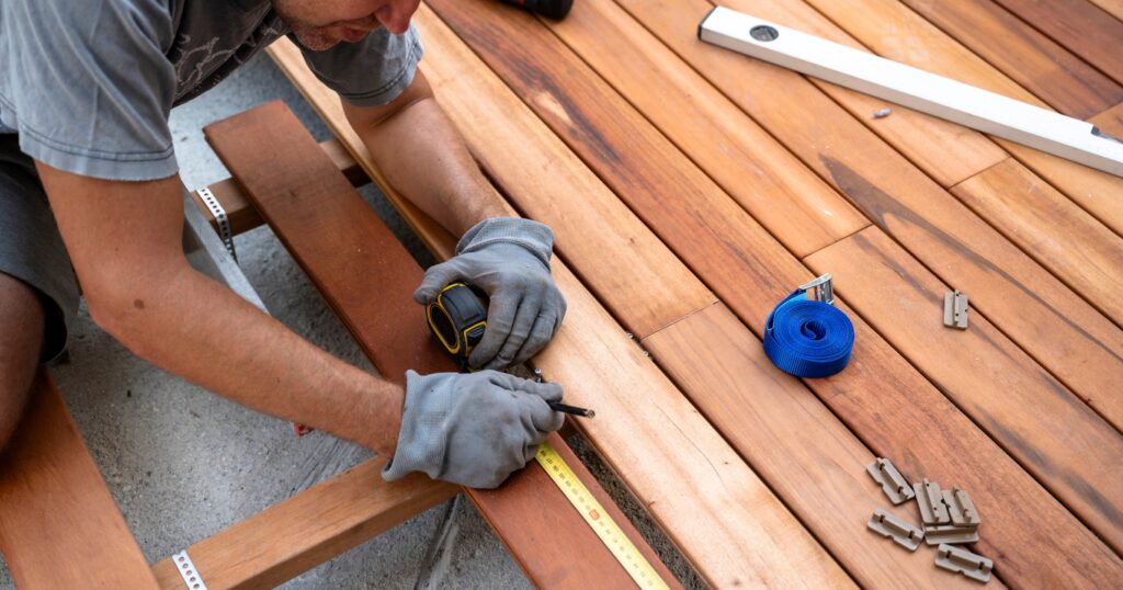 Deck Building ‣ Pathways Career College construction worker wearing gloves building a deck and measuring using a tape measure, level, and tools